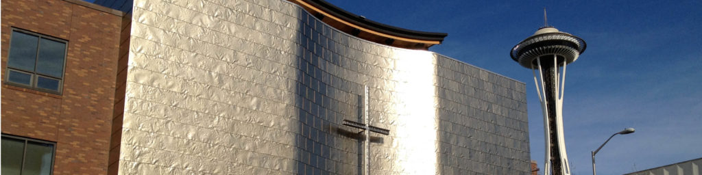 First Church Seattle exterior with large cross on white tile wall, brick section, and Seattle Space Needle visible in background under clear blue sky.