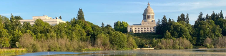 Washington State Capitol building with golden dome visible across a river, surrounded by evergreen trees and landscaping.