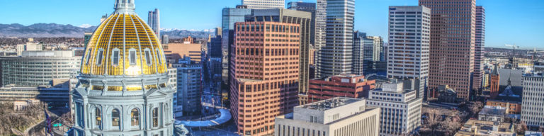 Denver city skyline featuring a prominent white domed building with gold roof and modern skyscrapers under clear blue sky.