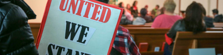 Church gathering showing a sign reading 'UNITED WE' on light blue and red background with church interior and congregation members seated in pews.