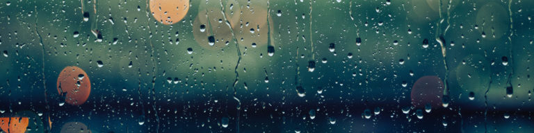 Raindrops and water on a window or glass surface with silhouettes visible through wet glass during rain.