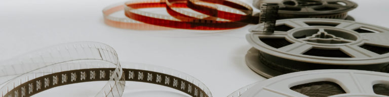 Close-up photo of vintage film reels and strips with red, white, and black film spools on white background.