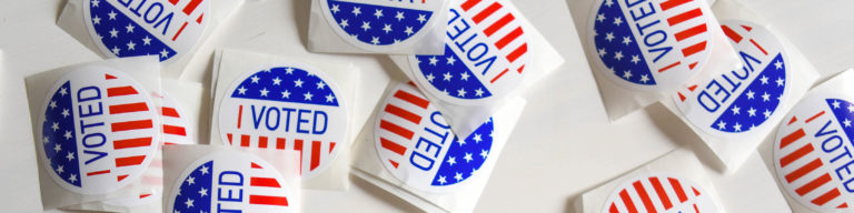 Multiple I Voted stickers arranged on white surface, featuring red and blue American flag design with text I VOTED.