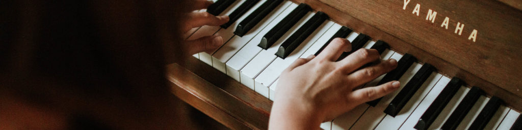 Hands playing a Yamaha piano keyboard in warm lighting with dark background, symbolizing Lent music and reflection.