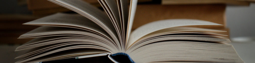 Close-up photograph of an open book with pages fanned out against a dark background, representing book club discussion and reading.