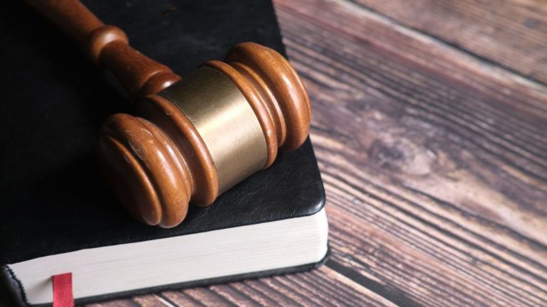 Close-up photograph of a wooden gavel resting on an open book on a wooden table, symbolizing law and justice.