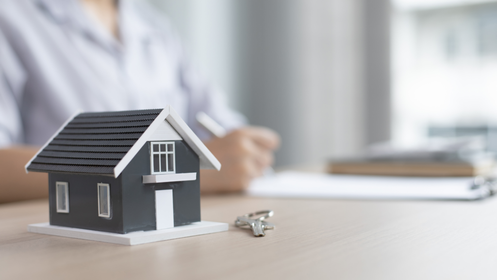 Small model house with a key displayed on a desk in front of a person, representing housing assistance or home support.