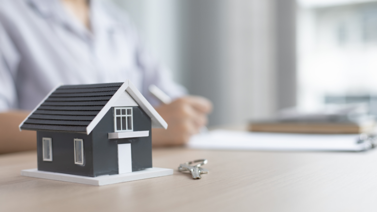 Small model house with a key displayed on a desk in front of a person, representing housing assistance or home support.