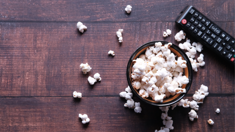 Bowl of popcorn with a remote control on a dark wooden surface, representing a movie screening or virtual event.