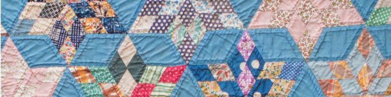 Colorful patchwork quilt banner with blue, pink, green, and orange fabric pieces in geometric diamond pattern.