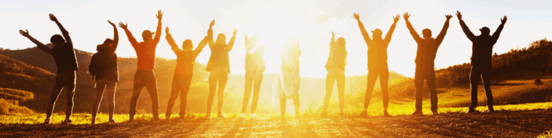 Group of silhouetted people with arms raised toward the sun against a golden sunset or sunrise landscape