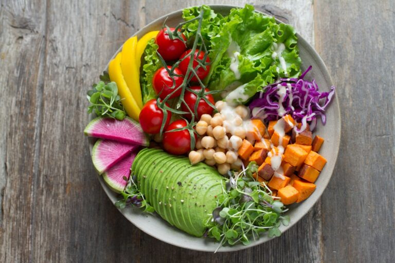 A colorful plant-based bowl of fresh vegetables, chickpeas, and avocado on a wooden table