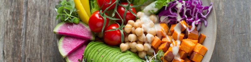 A colorful plant-based bowl of fresh vegetables, chickpeas, and avocado on a wooden table