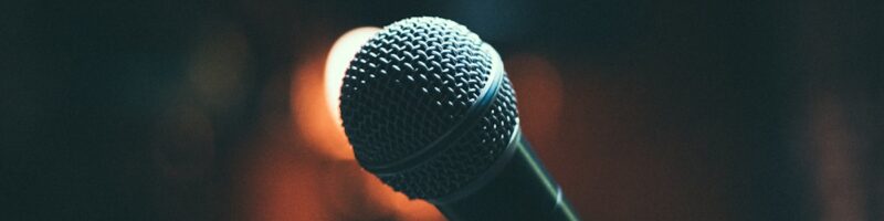 A microphone on a stand lit by warm stage lights, representing Open Mic Night