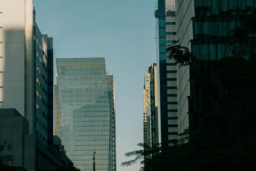Modern glass office towers rising above street trees in a city at dusk.