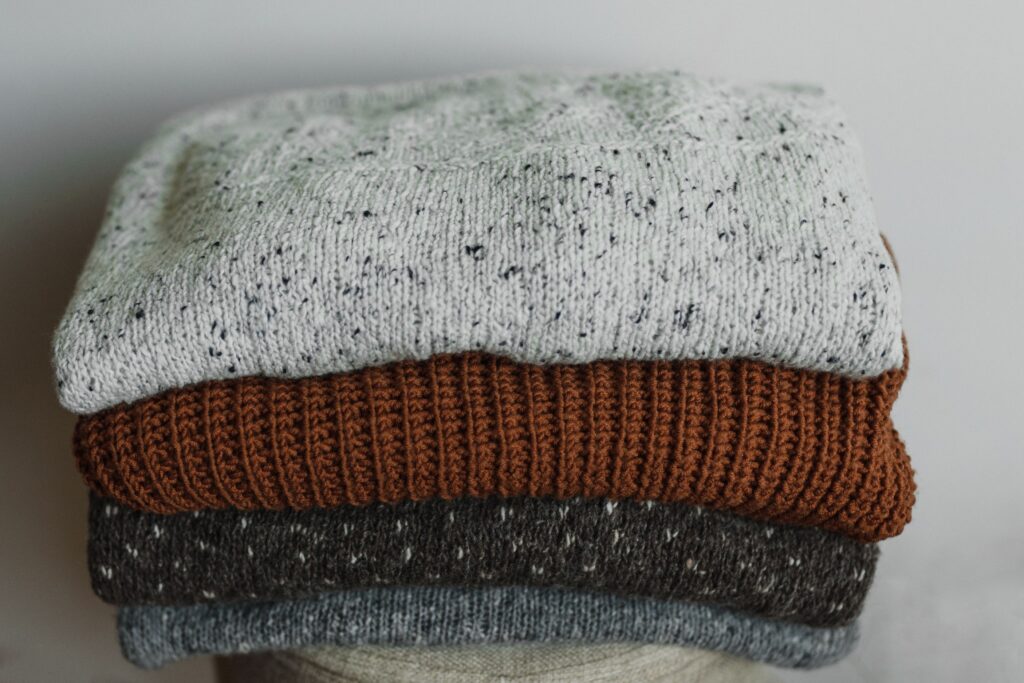 A neat stack of folded knitted sweaters in soft neutral and rust tones.
