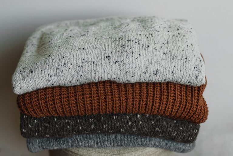 A neat stack of folded knitted sweaters in soft neutral and rust tones.