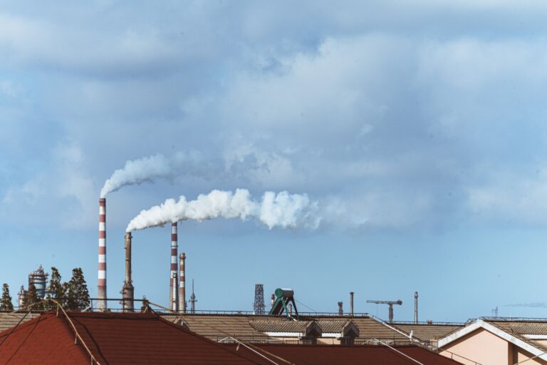 Factory chimneys emitting smoke over rooftops on a clear day, illustrating urban pollution.