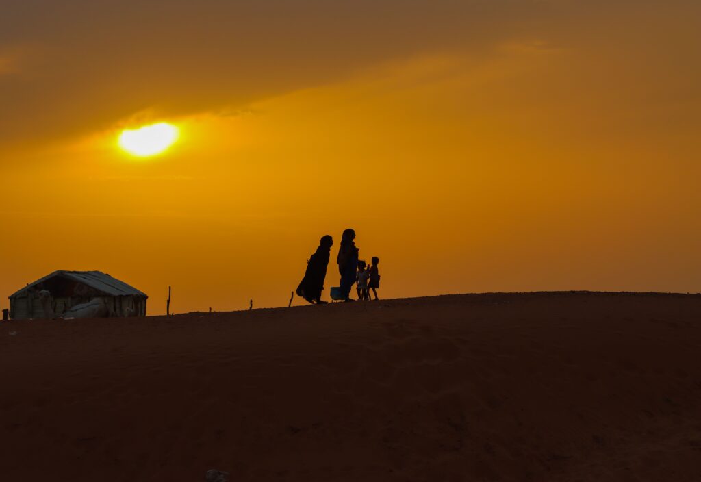 A family walks in silhouette across a sand dune at golden hour
