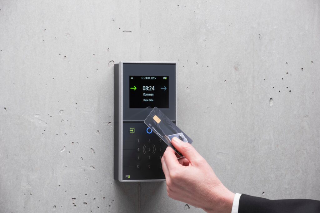 A hand holding an access fob card up to an electronic card reader beside a door.